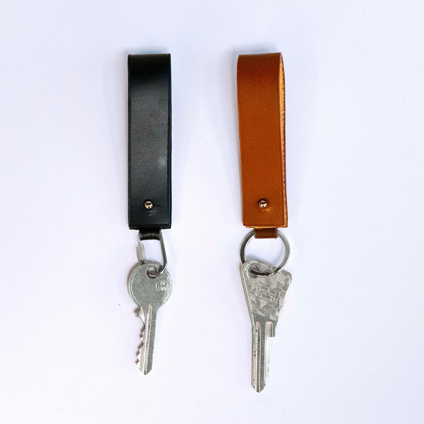 Minimal leather key holder — MODULE by atelier &LAB, black and cognac upcycled full-grain calf leather key holders with keys attached and carabiner clip, front view, Paris design studio.