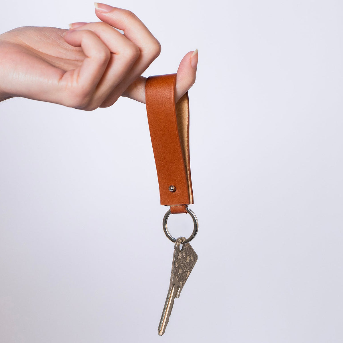 Minimal leather key holder — MODULE by atelier &LAB, cognac upcycled full-grain calf leather key holder held in hand with carabiner clip and keys attached, Paris design studio.