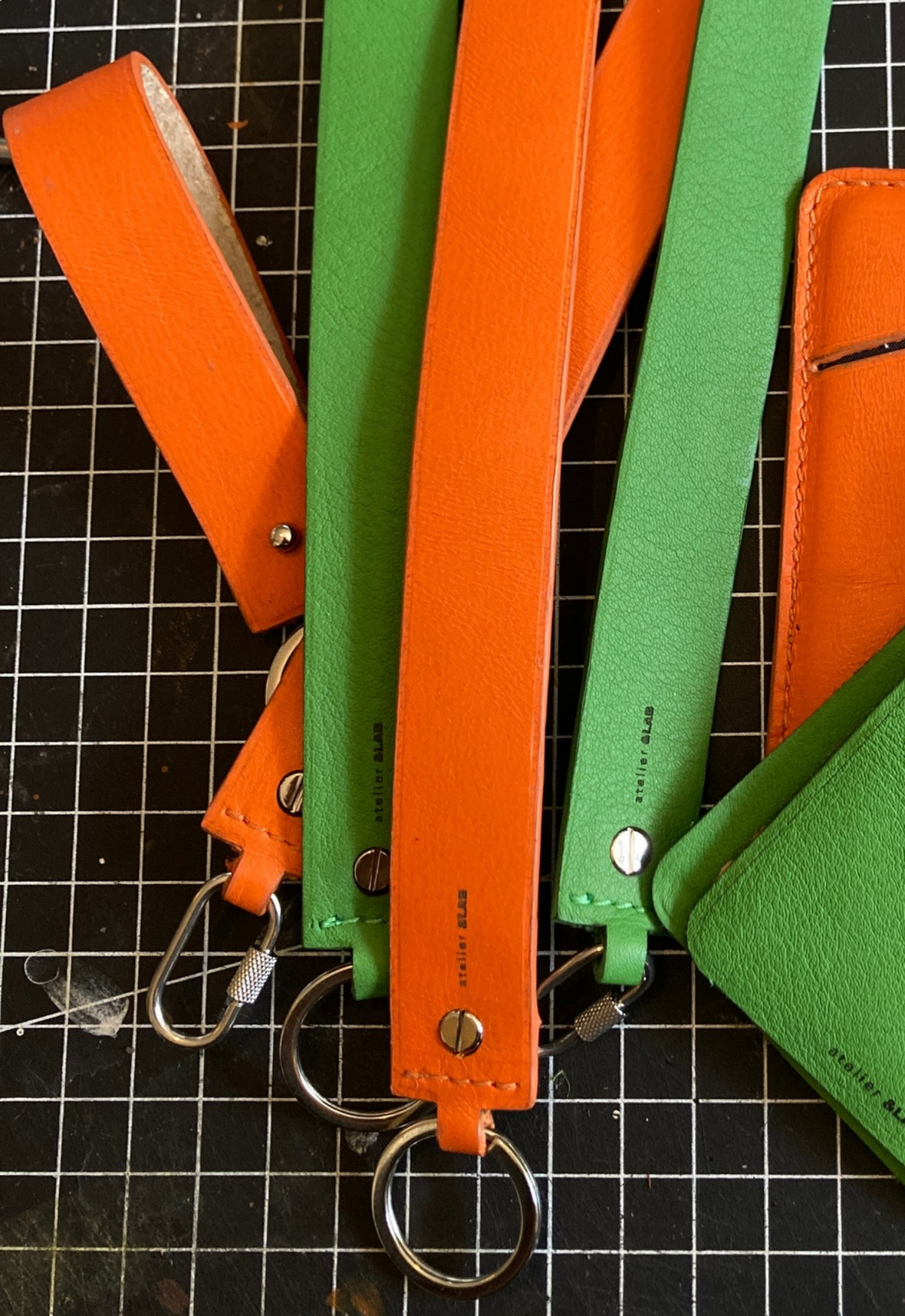Minimal leather key holders — MODULE by atelier &LAB in orange and green upcycled full-grain calf leather, with metal key rings, photographed on a workshop cutting mat.