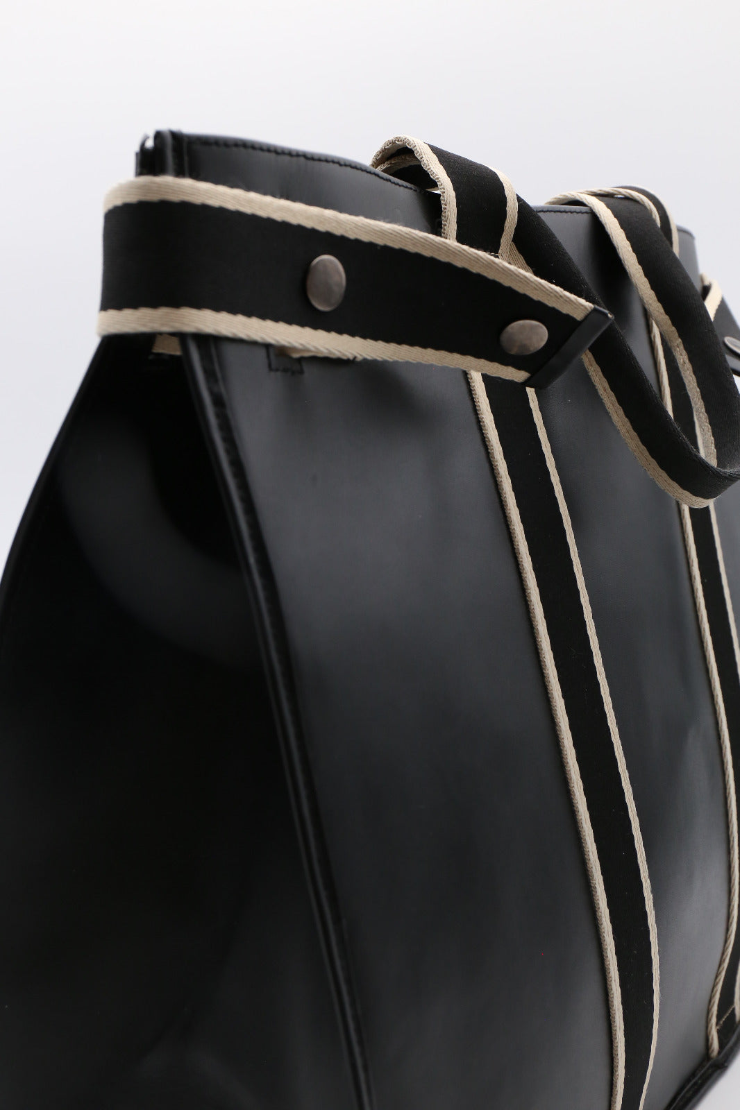 Close-up detail of NUMÉRO 00 MAXI by atelier &LAB in black leather, highlighting the strap with contrasting woven trim and metal rivets.