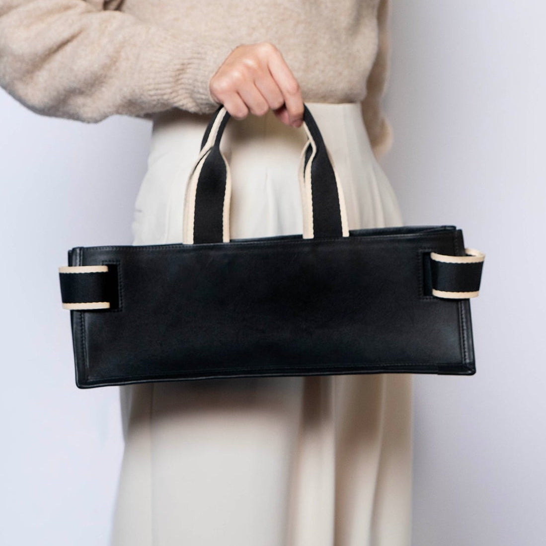 Minimal structured leather tote bag — NUMÉRO 02 PLAT by atelier &LAB, black upcycled full-grain calf leather, rear view handheld showing a clean flat structured shape for everyday use.