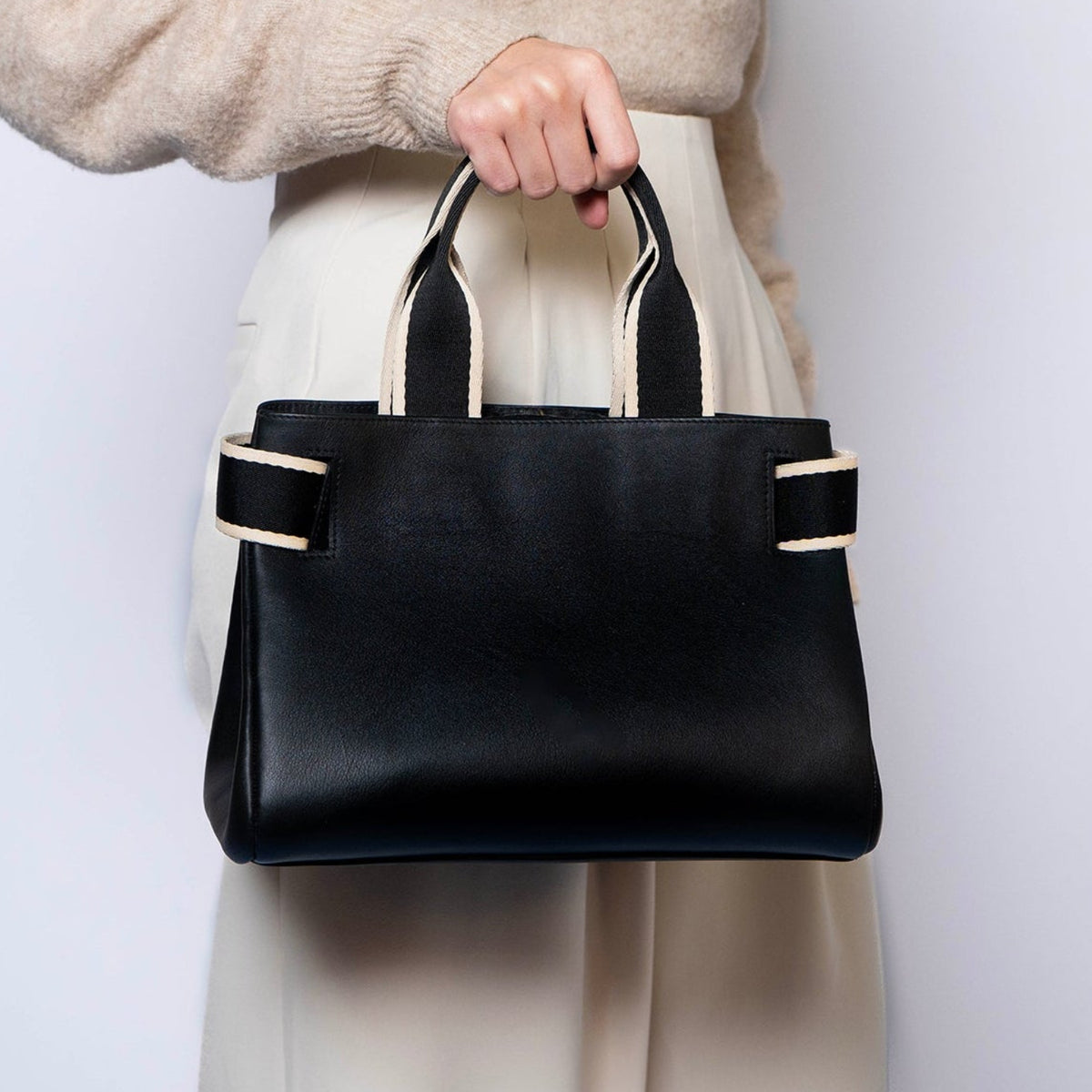 Structured leather handbag — NUMÉRO 04 by atelier &LAB, black upcycled full-grain calf leather, handheld rear view showing a compact graphic silhouette designed for hand carry.