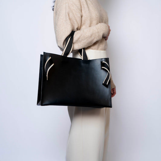 Lightweight structured black leather tote bag by atelier &LAB, worn on shoulder, architectural volume, minimalist studio photography