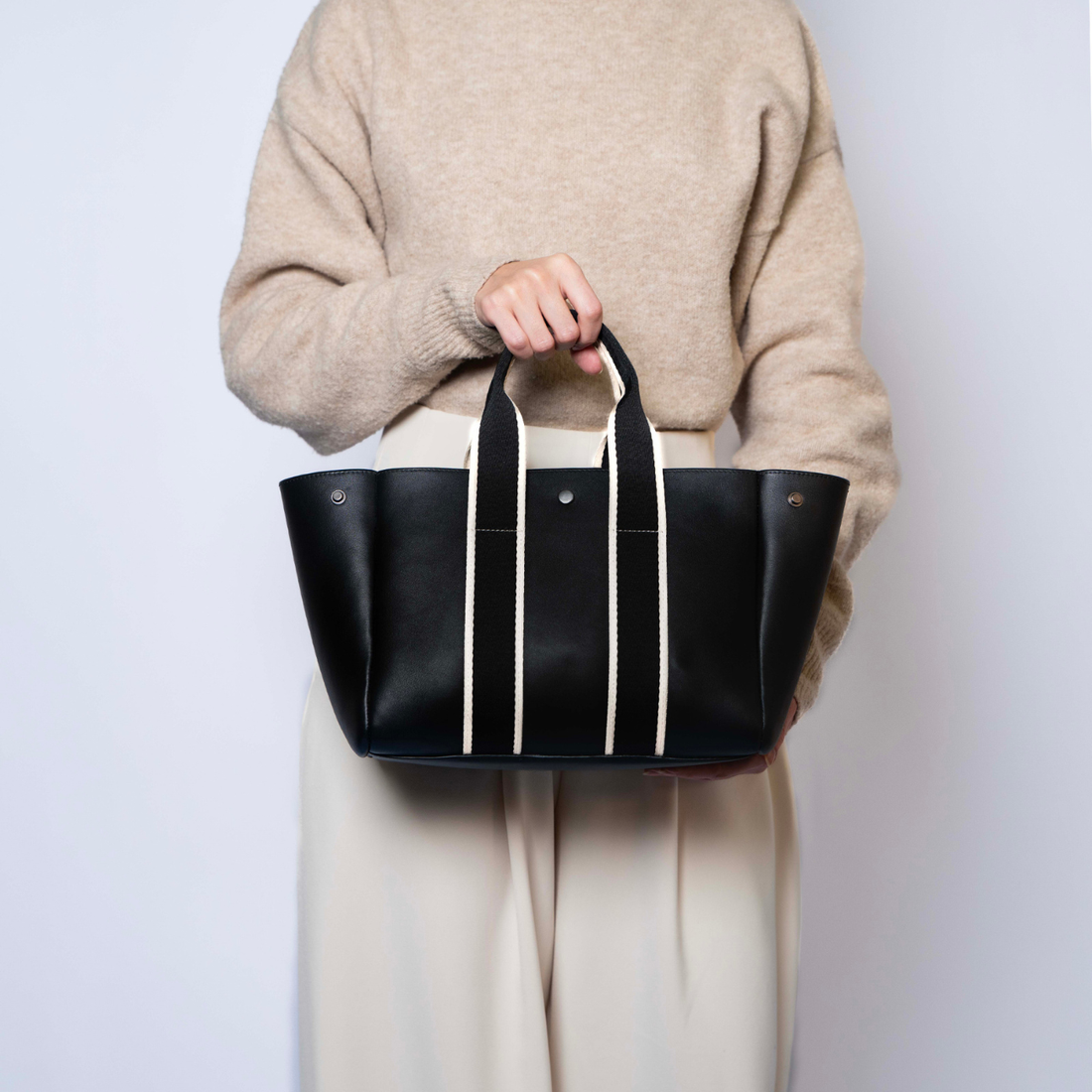 Person carrying the black NUMÉRO 03 Medium structured tote bag with ecru straps against a light background.