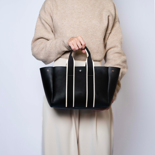 Person carrying the black NUMÉRO 03 Medium structured tote bag with ecru straps against a light background.