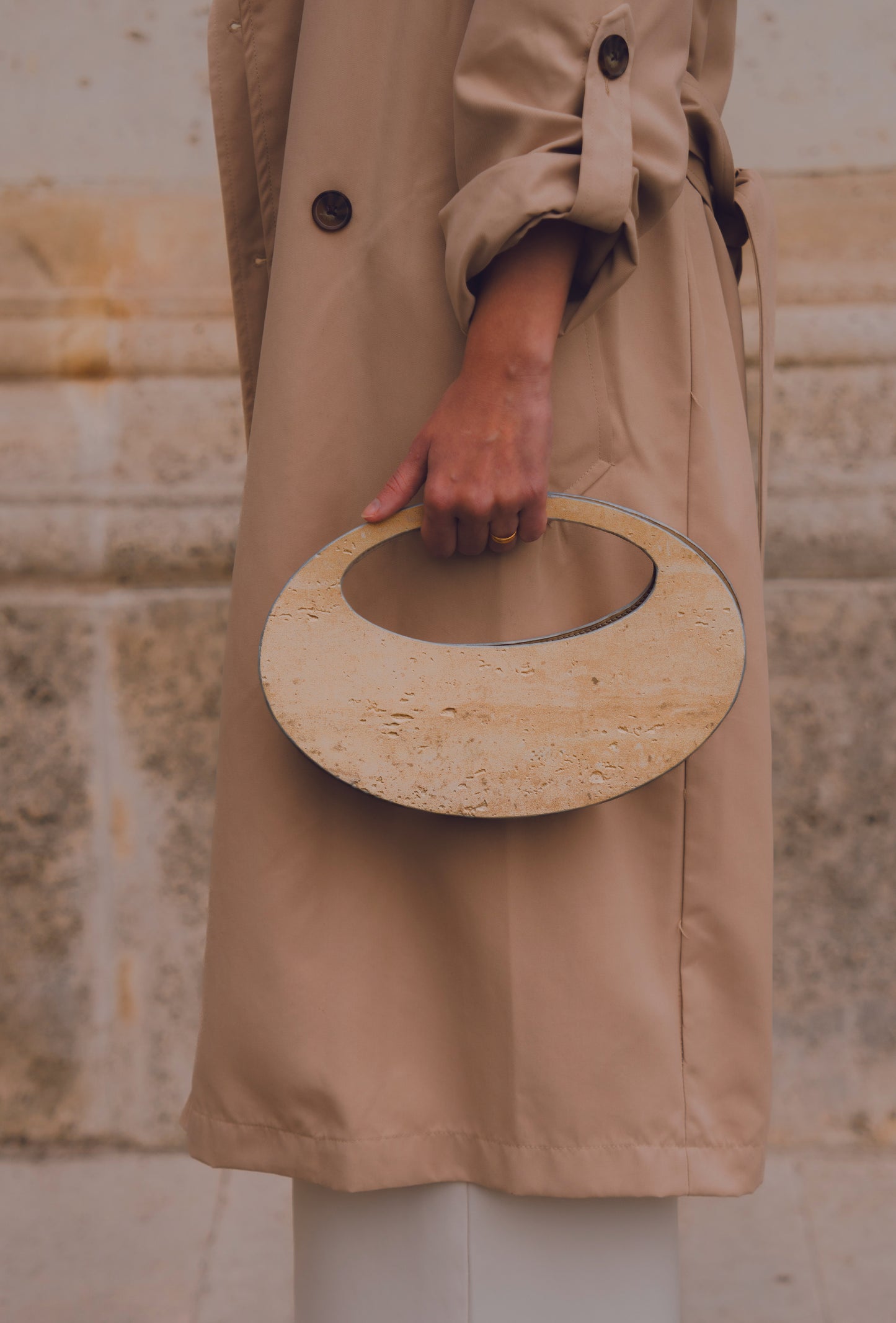 Close-up of ARCHIVE 01 by atelier &LAB — circular mineral composite (stone-based material) bag with integrated mineral handle and premium beige leather insert, worn in an editorial architectural setting at the Louvre, Paris.