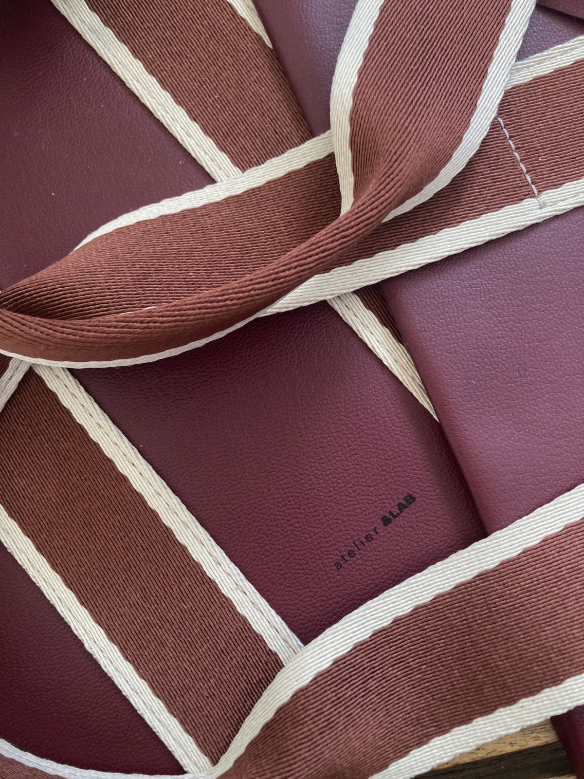 Detail of burgundy full-grain leather and contrasting textile straps on an atelier &LAB bag.