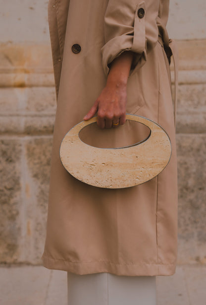 Close-up of ARCHIVE 01 by atelier &LAB — circular mineral composite (stone-based material) bag with integrated mineral handle and premium beige leather insert, worn in an editorial architectural setting at the Louvre, Paris.
