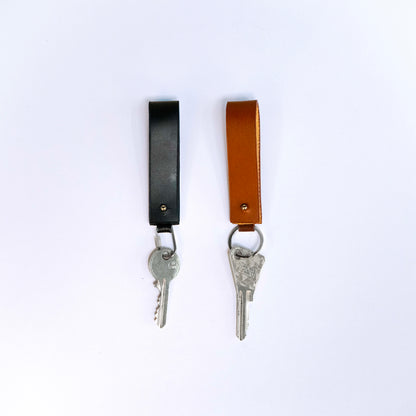 MODULE key holder by atelier &LAB — front view with keys, revealing a compact, architectural leather form in black and cognac with key ring and carabiner clip, premium upcycled full-grain calf leather.