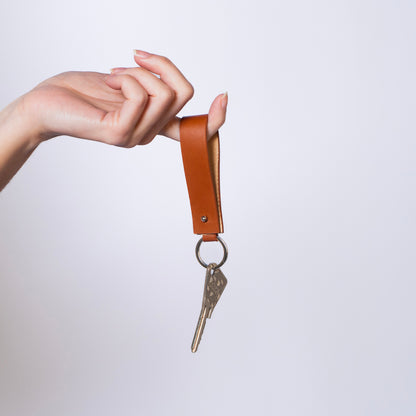 Minimal leather key holder — MODULE by atelier &LAB, cognac upcycled full-grain calf leather key holder held in hand with carabiner clip and keys attached, Paris design studio.