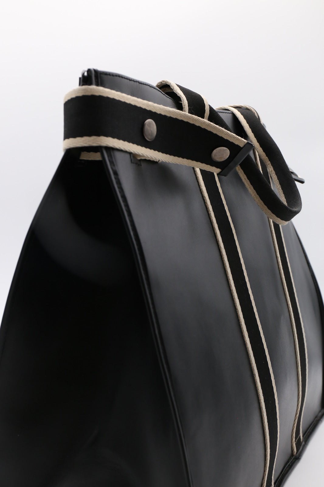 Close-up detail of NUMÉRO 00 Maxi by atelier &LAB in black leather, highlighting the strap with contrasting woven trim and metal rivets on a structured, architectural volume.