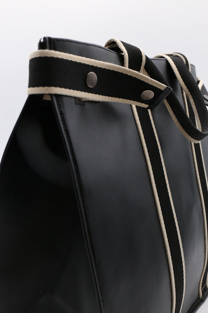 Close-up detail of NUMÉRO 00 MAXI by atelier &LAB in black leather, highlighting the strap with contrasting woven trim and metal rivets.