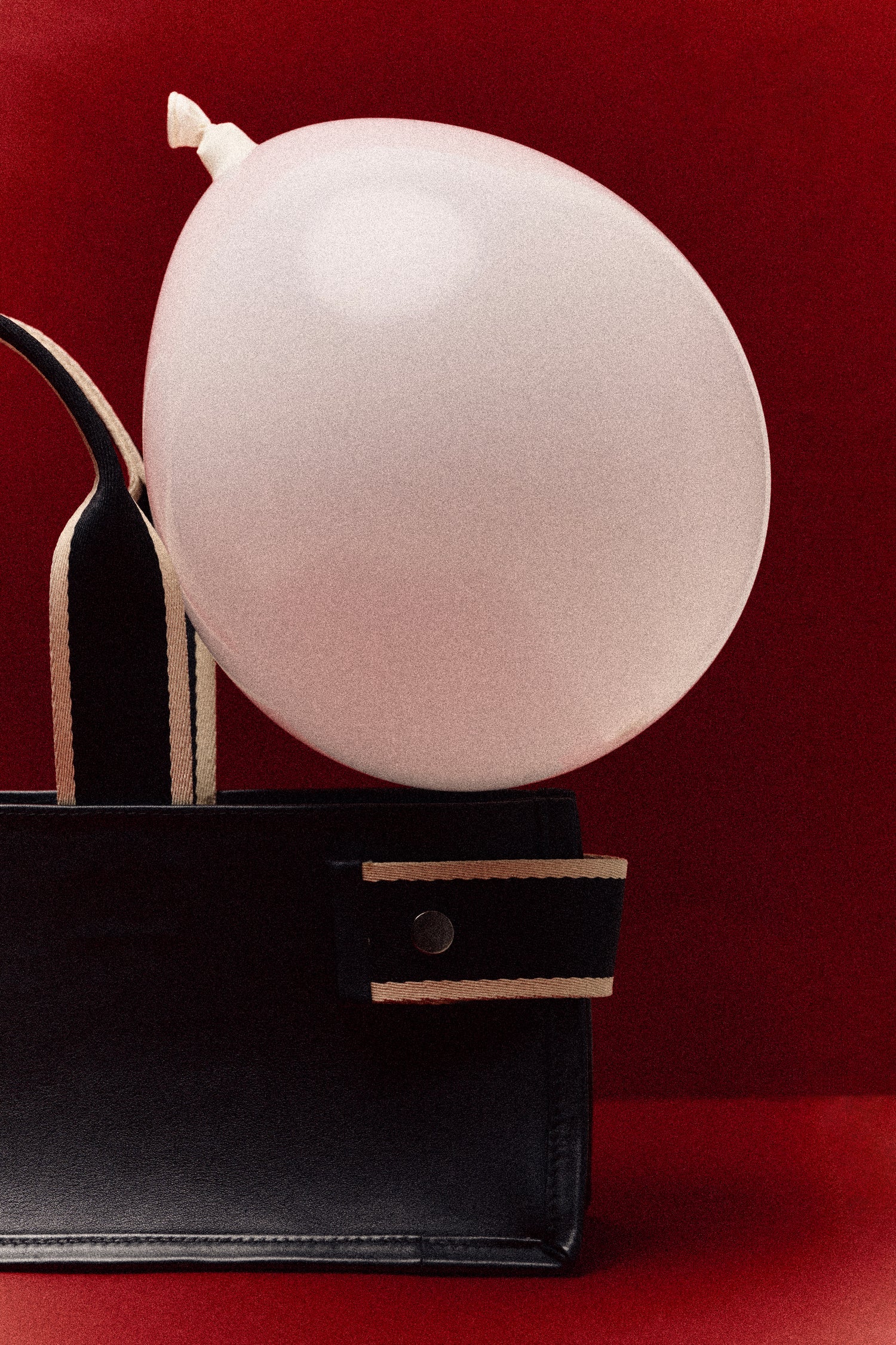 Structured leather tote bag detail — NUMÉRO 01 by atelier &LAB, black leather and contrast straps with balloon on deep red background