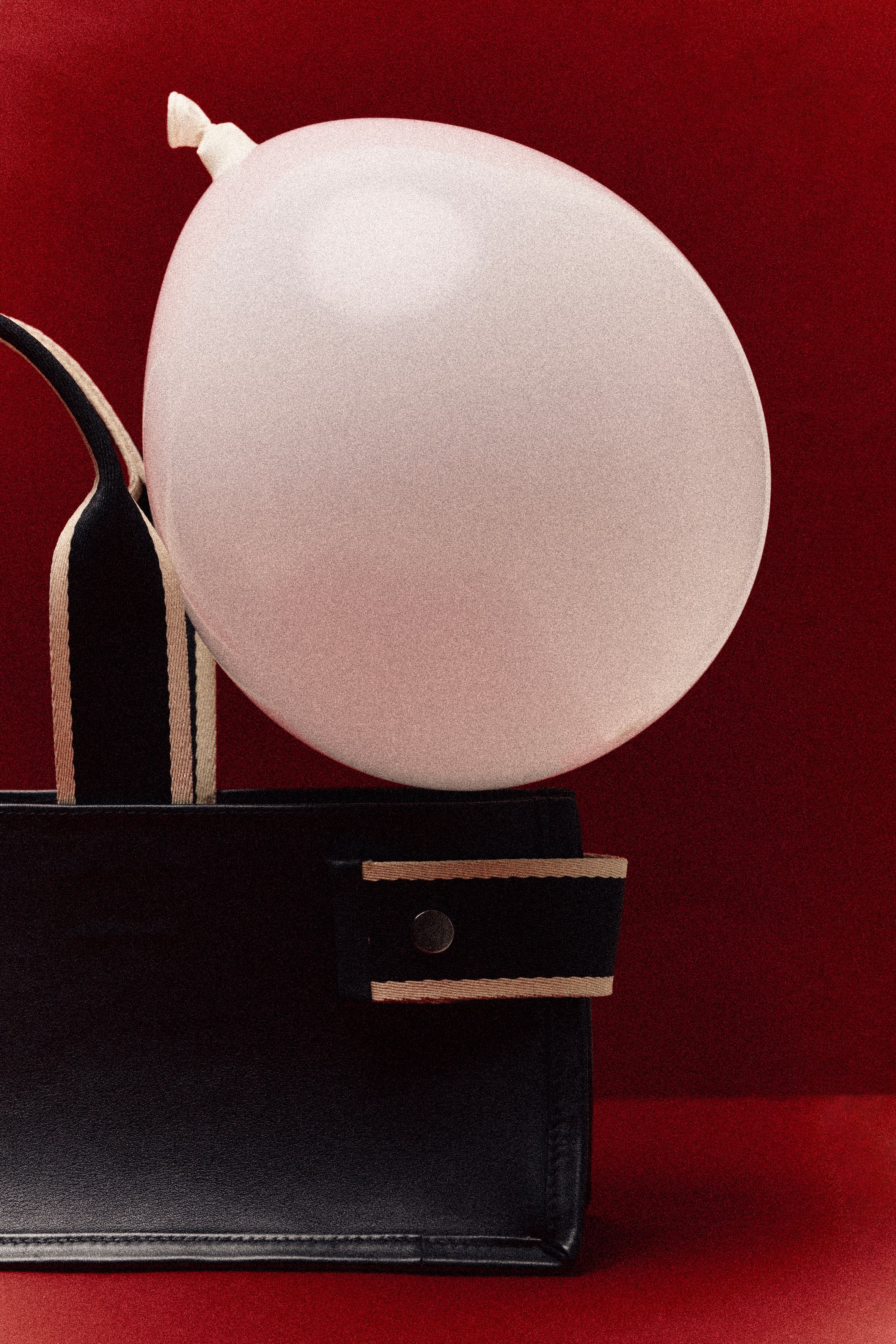 Structured leather tote bag detail — NUMÉRO 01 by atelier &LAB, black leather and contrast straps with balloon on deep red background
