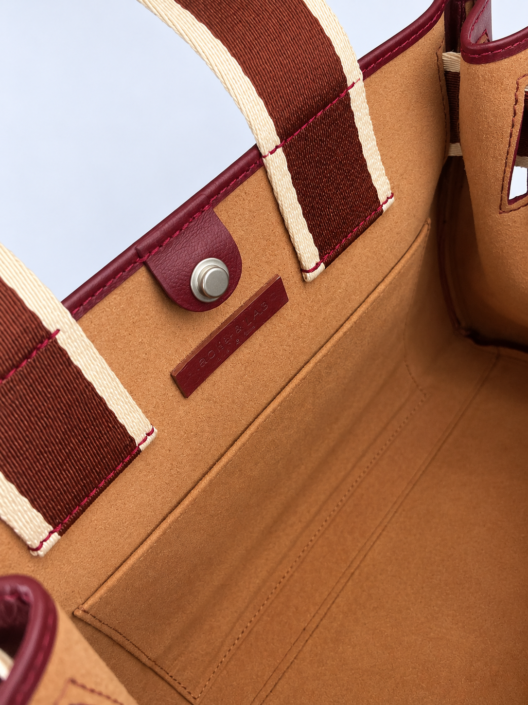 Interior detail of the NO04 M Bordeaux leather handbag by Hiroki AMANO — atelier &LAB, showing the cognac suede lining, stitched interior pocket, magnetic snap closure and contrasting woven handles. Designed and made near Paris.