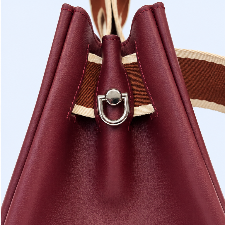 Close-up of the NO04 M Bordeaux handbag by Hiroki AMANO — atelier &LAB, showing the silver-tone D-ring attachment, folded calf leather side panels, tonal stitching and contrasting rust and ecru woven strap.